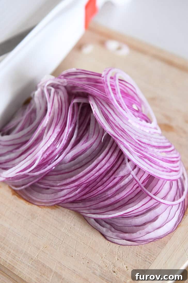Thinly sliced red onions off a mandoline slicer on wood cutting board.