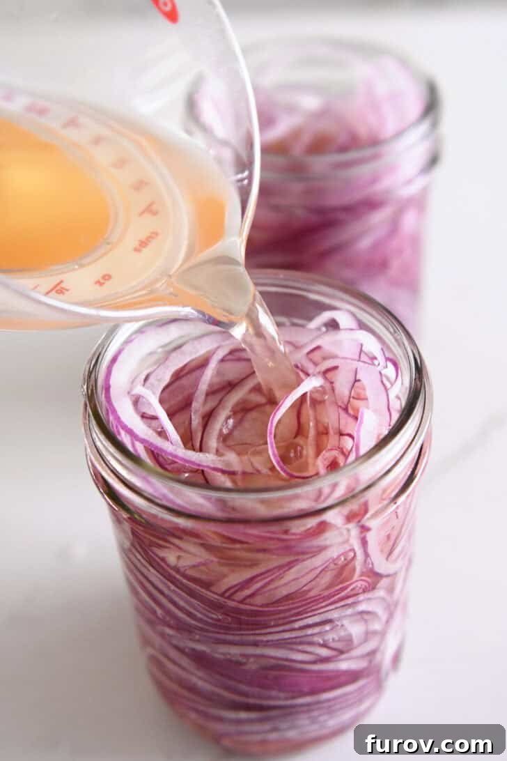 Pouring vinegar, salt and sugar in jar of thinly sliced red onions.