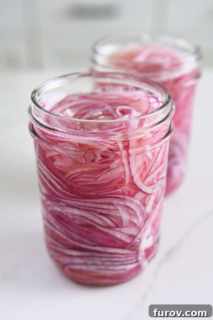Two pint jars with thinly sliced red onions and vinegar.