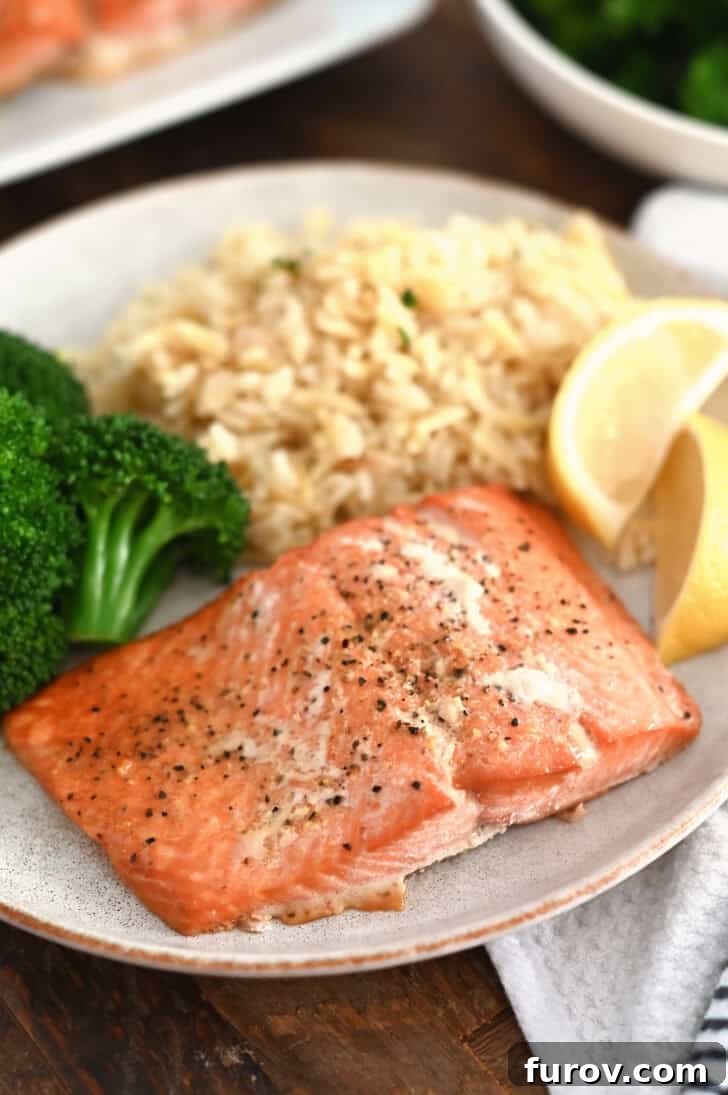 Perfectly baked salmon fillet on a gray plate, garnished with fresh lemon slices, accompanied by tender cooked broccoli and fluffy rice pilaf.