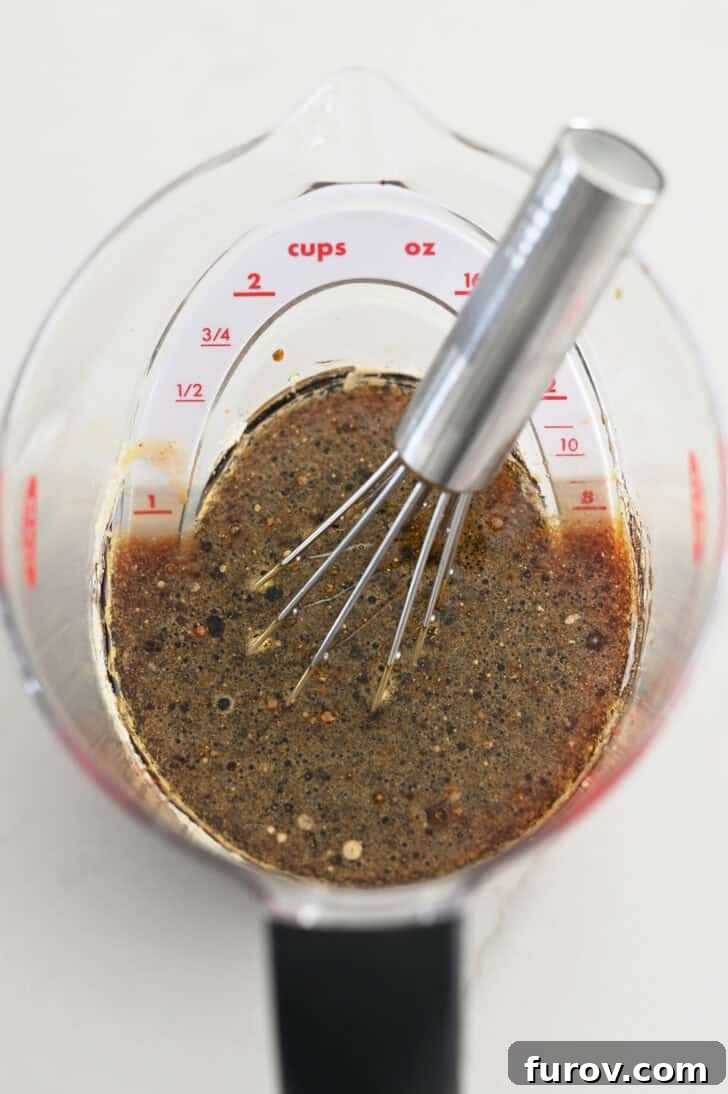 Top-down view of a clear liquid measuring cup holding a small whisk, with soy sauce and brown sugar visible, ready for mixing the marinade.