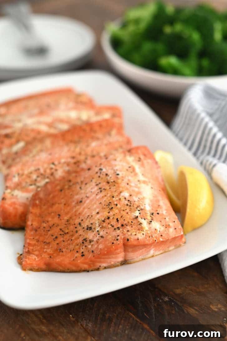 Three perfectly baked salmon fillets, elegantly arranged on a white platter and garnished with vibrant lemon slices, showcasing their golden-brown crust.