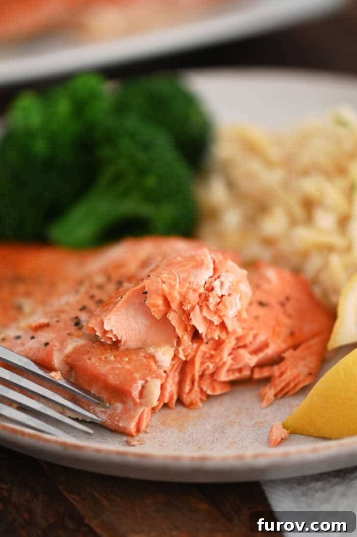 A perfectly cooked salmon fillet on a gray plate, accompanied by a fork, fluffy rice pilaf, and steamed broccoli, showcasing a complete and healthy meal.