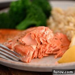 Baked salmon on a gray plate, garnished with fresh lemon wedges, alongside cooked broccoli and rice pilaf, highlighting the meal's appeal.