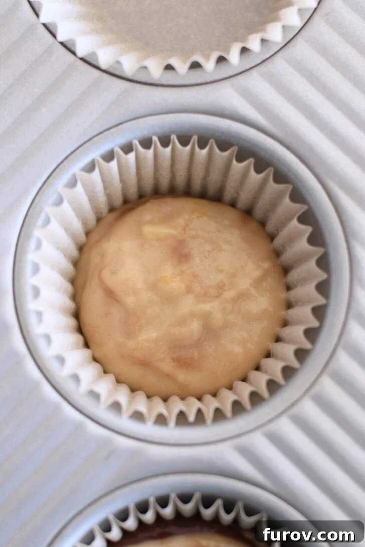 Marbled Chocolate Banana Muffins 7 A paper-lined muffin tin, with a careful scoop of light-colored banana muffin batter placed at the bottom, ready for the next layer.