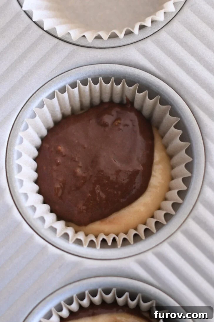 Marbled Chocolate Banana Muffins 8 A muffin tin liner showing the first layer of banana muffin batter, topped with a smaller scoop of dark chocolate banana muffin batter, illustrating the initial layering step.