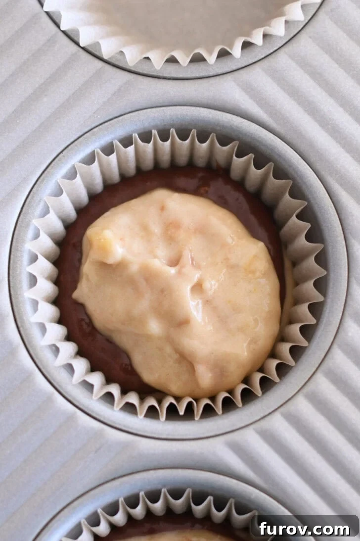 Marbled Chocolate Banana Muffins 9 A muffin tin liner with alternating layers of banana muffin batter and chocolate banana muffin batter, showing the progression of the swirl assembly.