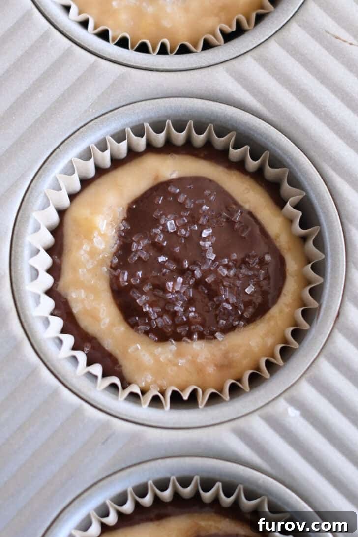 Marbled Chocolate Banana Muffins 10 A lined muffin tin filled with layered banana and chocolate batter, generously sprinkled with coarse sugar, ready for baking.