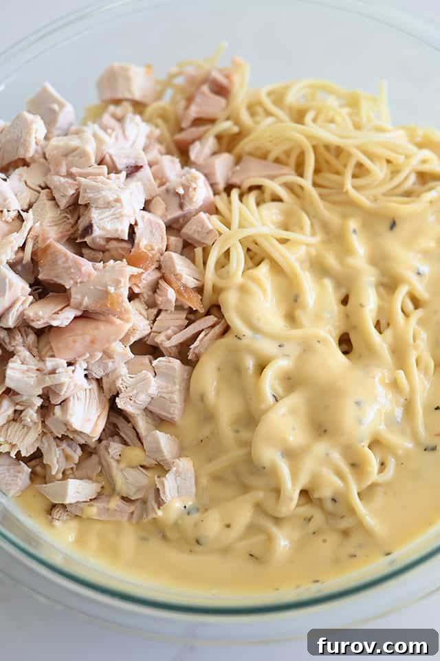 Glass bowl with cooked spaghetti noodles, cooked chicken, and homemade cheese sauce.