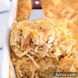 Spatula holding square of cheesy chicken spaghetti in white pan with the rest of the casserole.