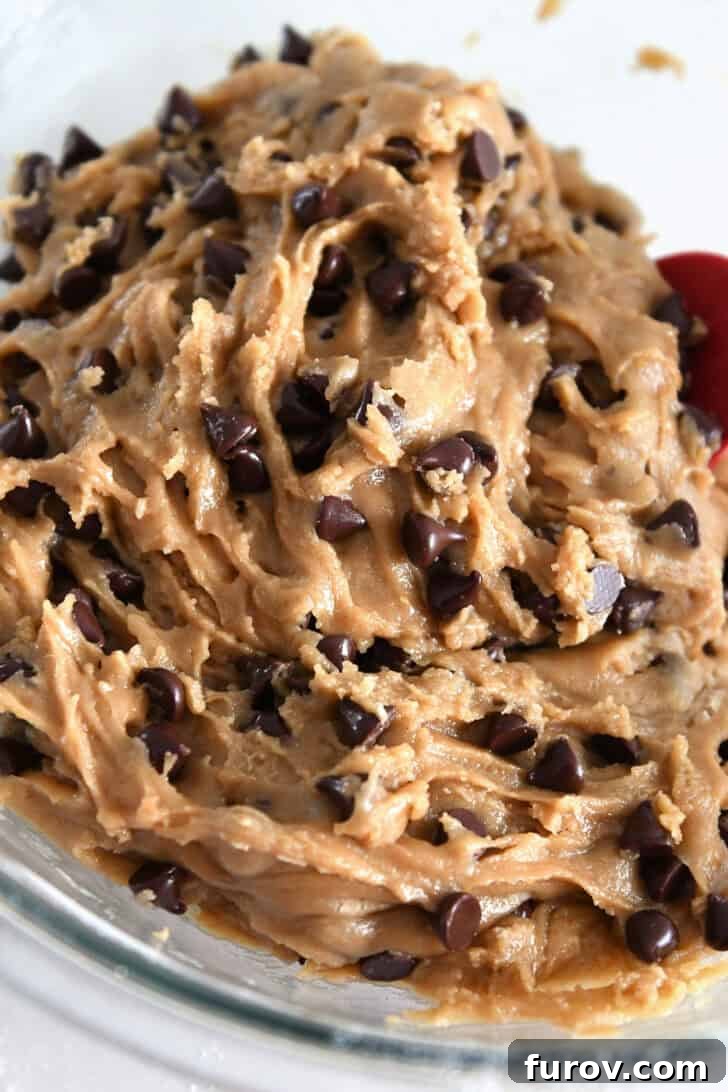 A bowl of rich, unbaked chocolate chip cookie dough, studded with chocolate chips, ready for baking.