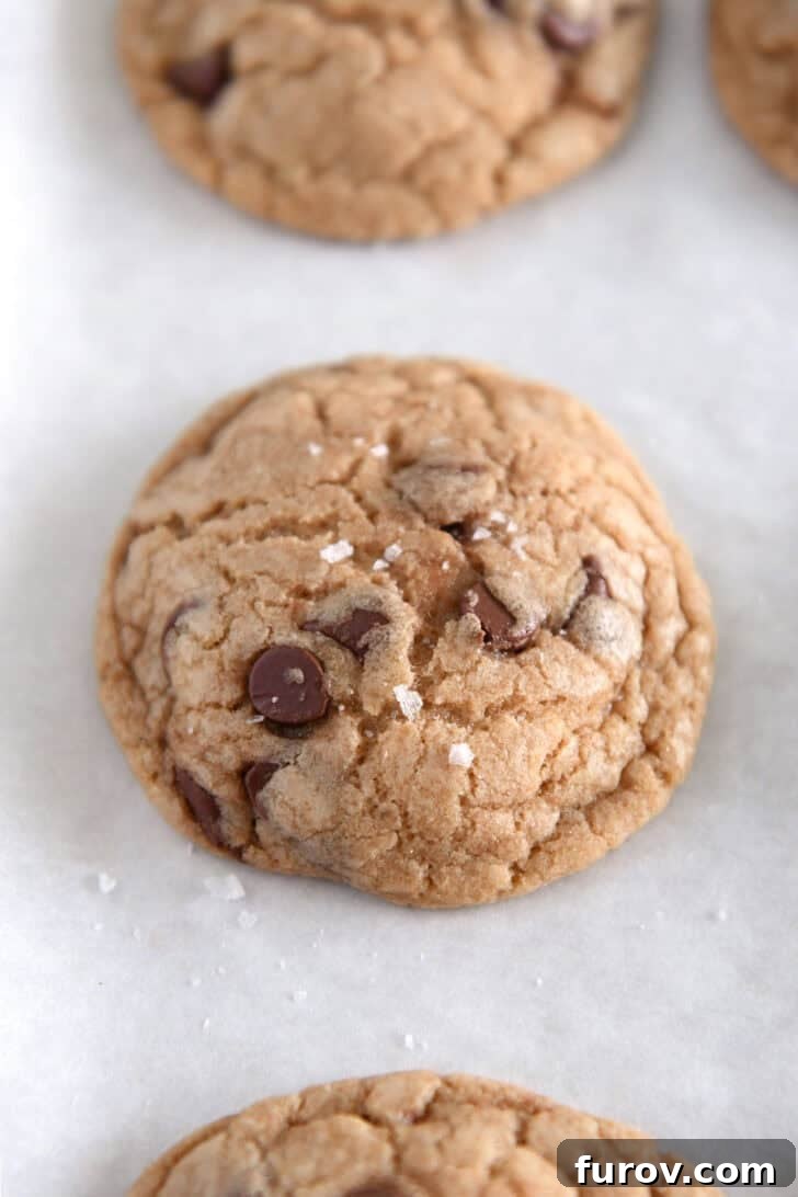 Baked brown butter chocolate chip cookies on a parchment-lined baking sheet, lightly sprinkled with flaky sea salt.