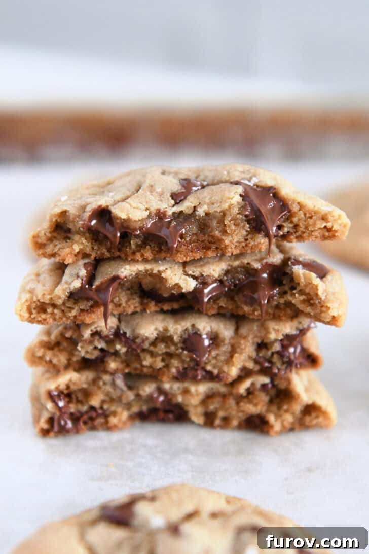 Four half cookies, showcasing their soft interior and melty chocolate chips, stacked on each other on a parchment-lined baking sheet.