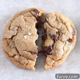 Soft melty brown butter chocolate chip cookie split in half on parchment paper.
