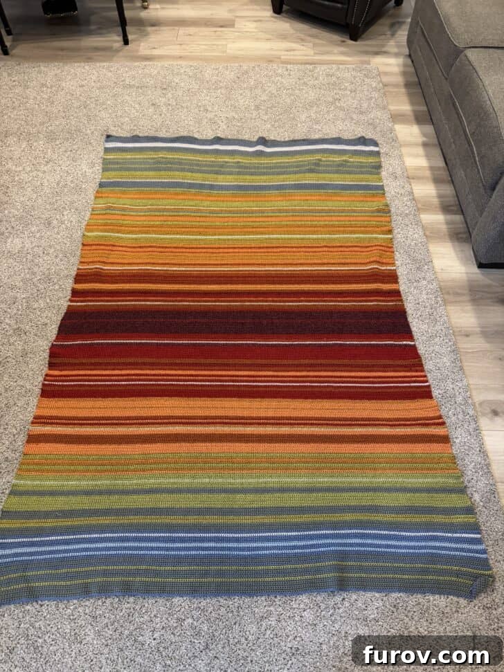 A completed crocheted temperature blanket, displaying a beautiful gradient of colors, laid out flat on a carpet.