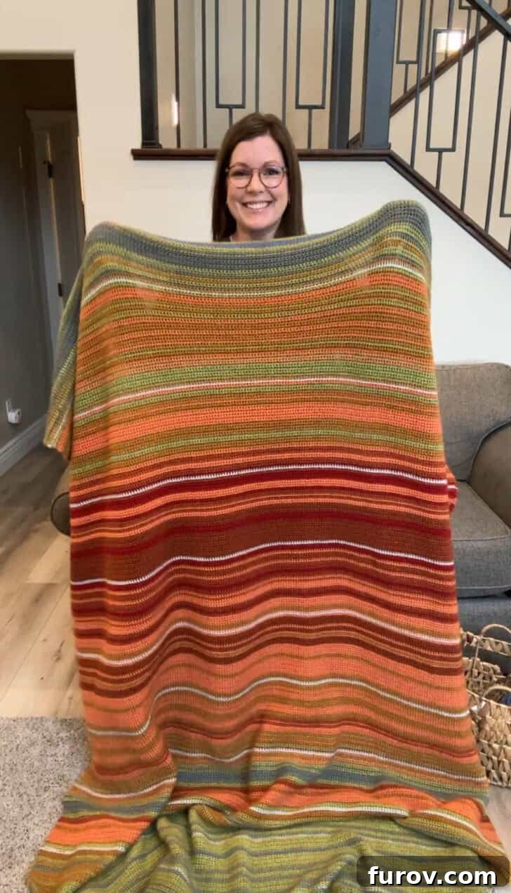 Mel proudly holding her second finished crocheted temperature blanket, representing the weather in Switzerland.