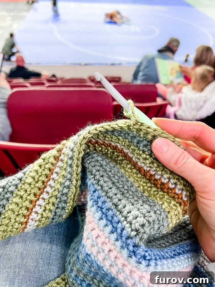 Close-up of hands crocheting vibrant green stripes onto a temperature blanket, showing detailed stitch work.