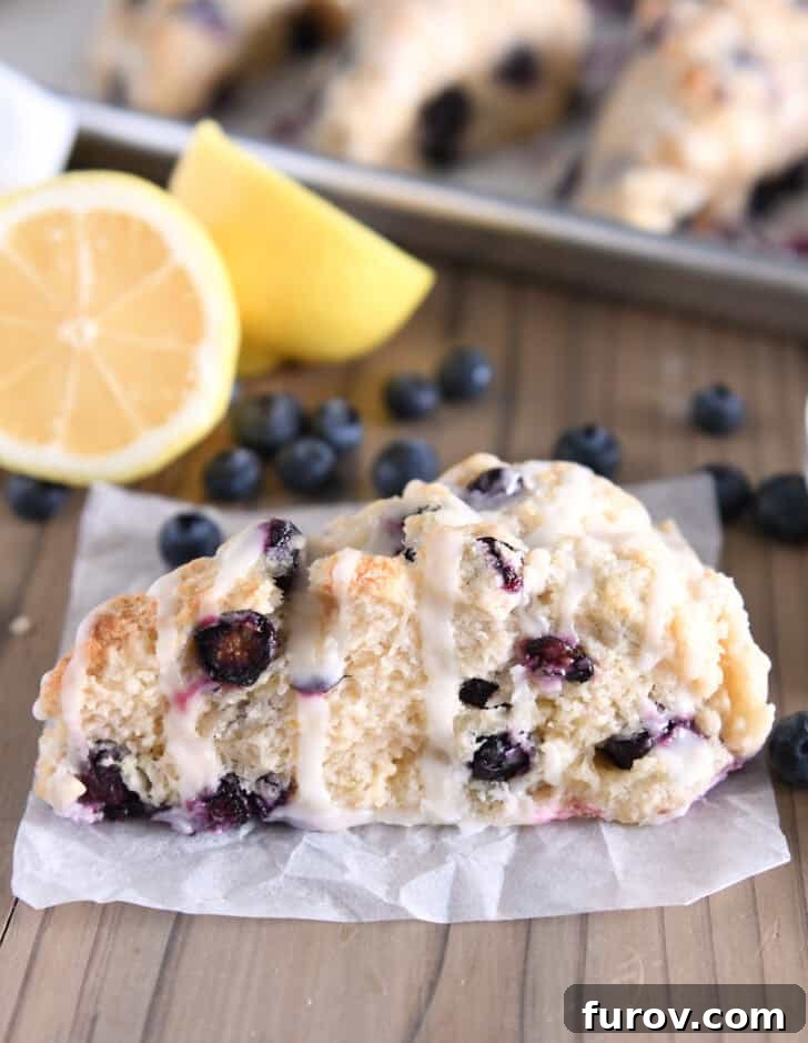 A single, perfectly baked and glazed triangle-shaped lemon blueberry scone resting on crumpled white parchment paper, highlighting its delicious texture.