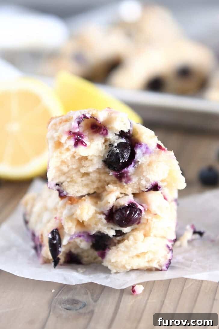 Two halves of a perfectly baked lemon blueberry scone, stacked on white parchment paper, revealing its flaky interior and juicy blueberries.
