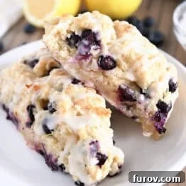 Two baked and glazed lemon blueberry scones on a white plate, ready to be enjoyed.