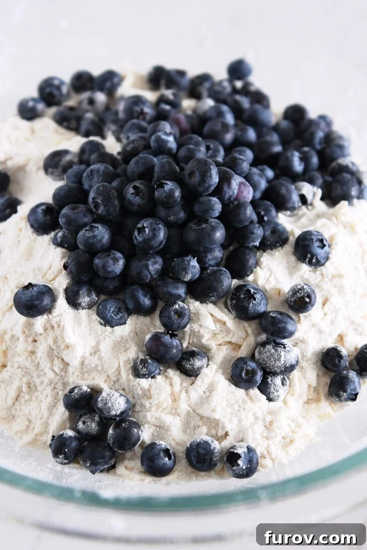 Fresh, vibrant blueberries nestled in a bowl with grated butter shreds and dry scone ingredients, ready for mixing.
