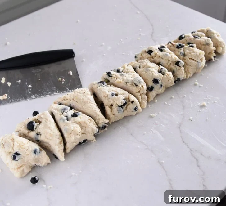Scone dough expertly cut into triangular pieces on a floured surface with a bench scraper, ready for baking.
