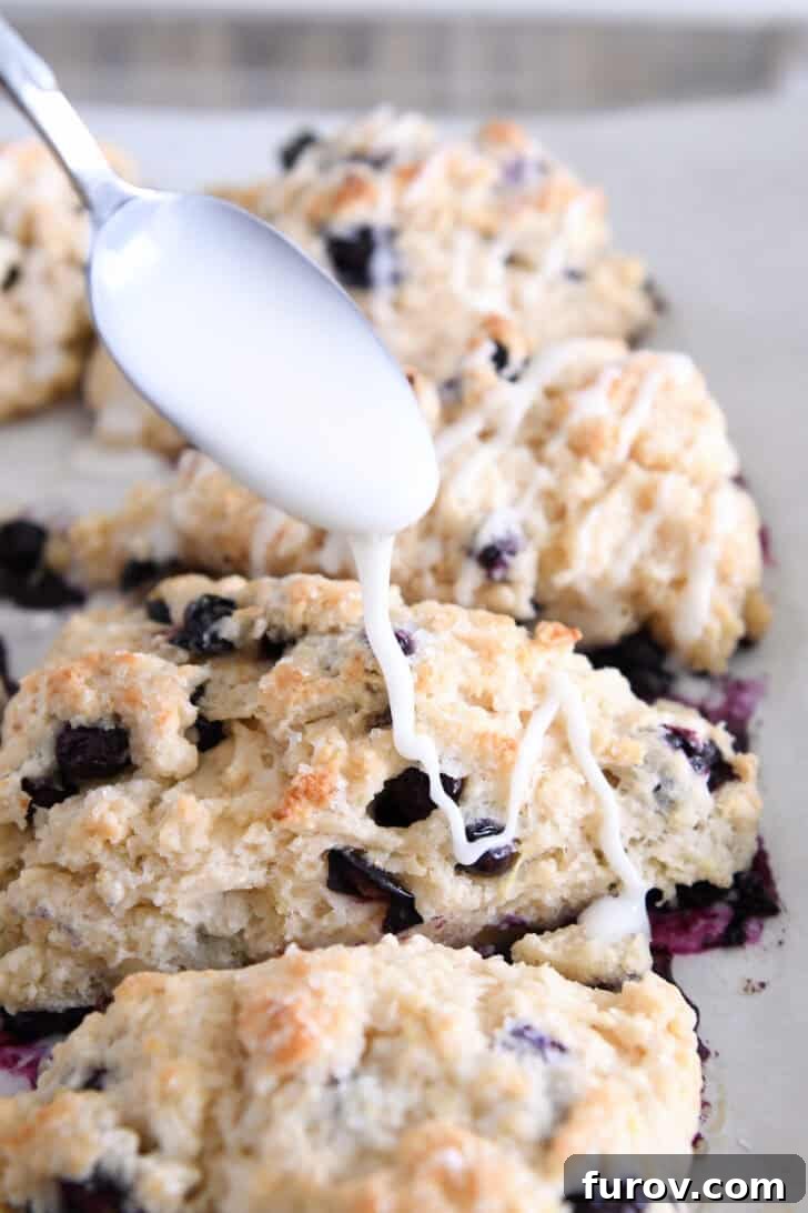 A stream of vibrant lemon glaze being drizzled artfully over freshly baked lemon blueberry scones, creating a beautiful finish.