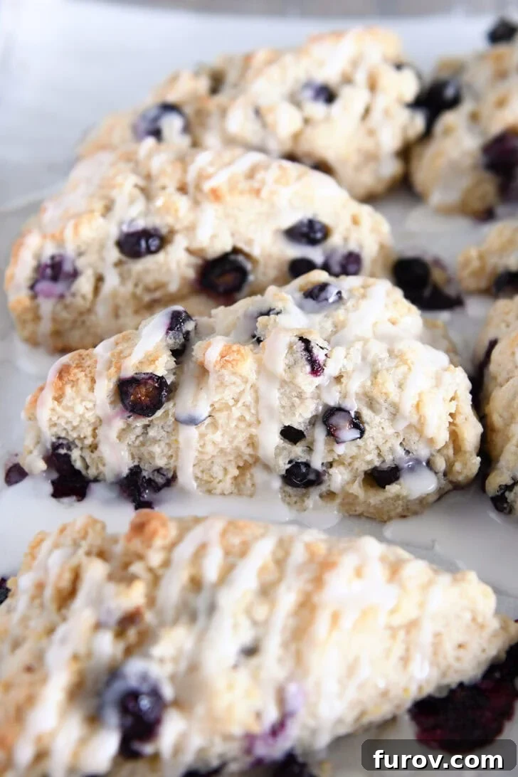 A collection of glazed, baked lemon blueberry scones artfully arranged on a parchment-lined baking sheet, showcasing their golden-brown crusts.