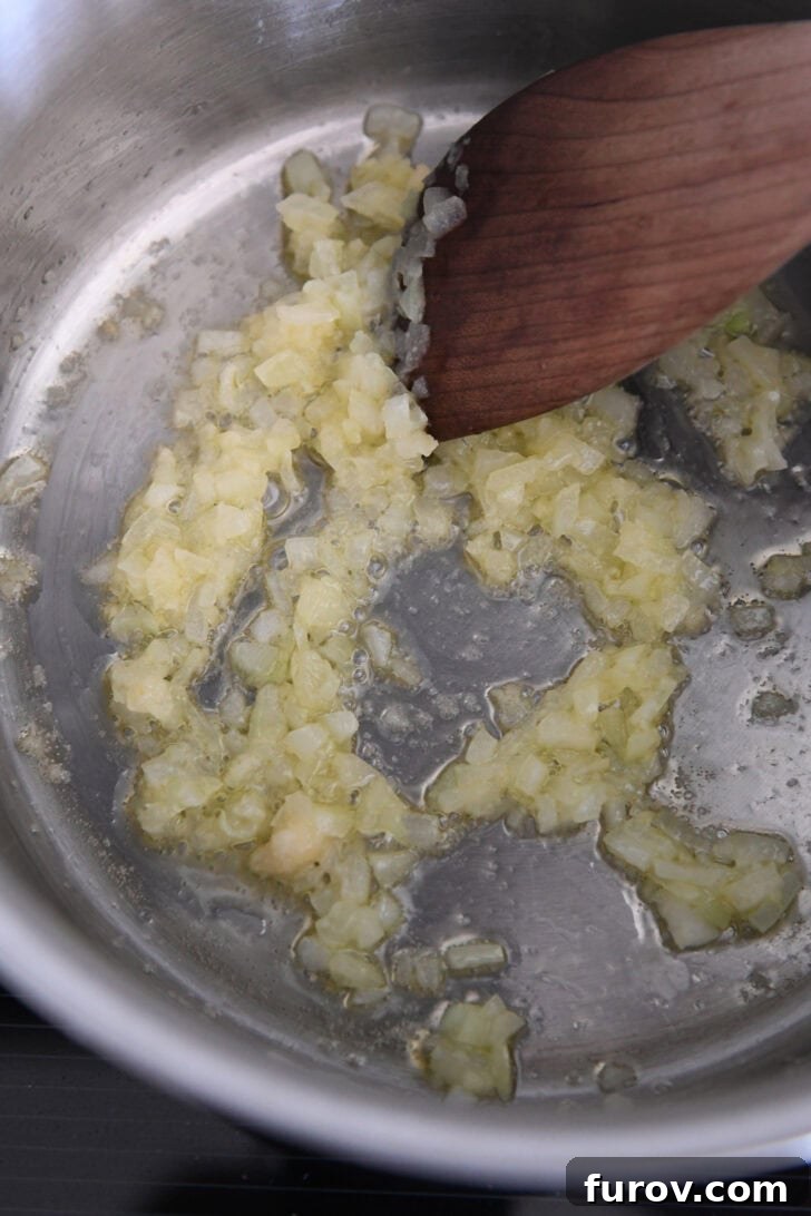 Finely chopped garlic and onions being sautéed in olive oil in a stainless steel pot, creating a fragrant base for the refried beans.