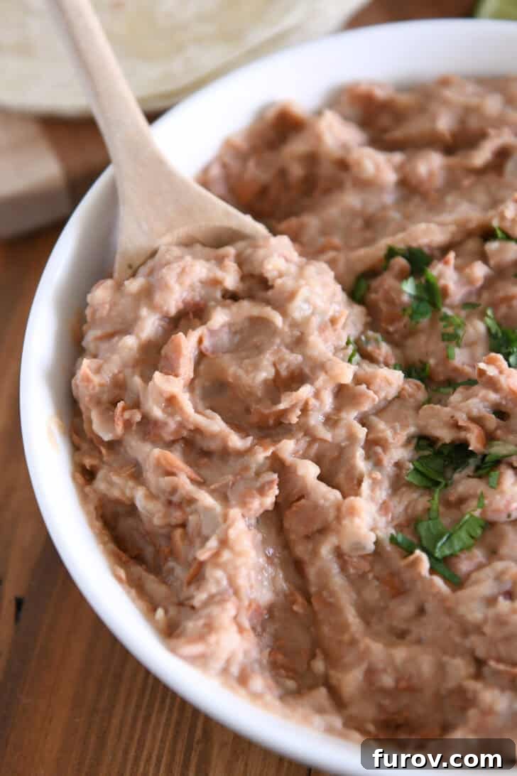 A wooden spoon delicately scooping a generous serving of creamy refried beans from a white bowl, ready to be enjoyed as a perfect side dish.