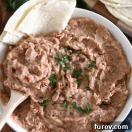 Top down view of white bowl with easy refried beans, garnished with fresh cilantro and served alongside tortillas.
