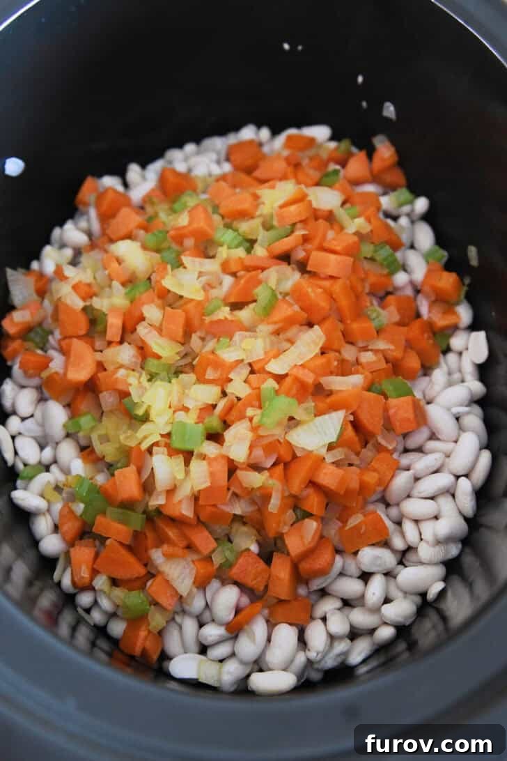 Slow cooker filled with dry white beans, diced carrots, celery, and onions, ready for the broth.