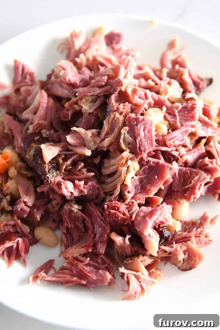 Perfectly shredded ham pieces on a white plate, ready to be added back to the soup.