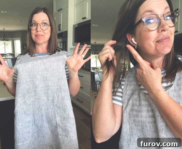 Woman in apron in kitchen pointing to earbuds in ears, happily listening to an audiobook while cooking.