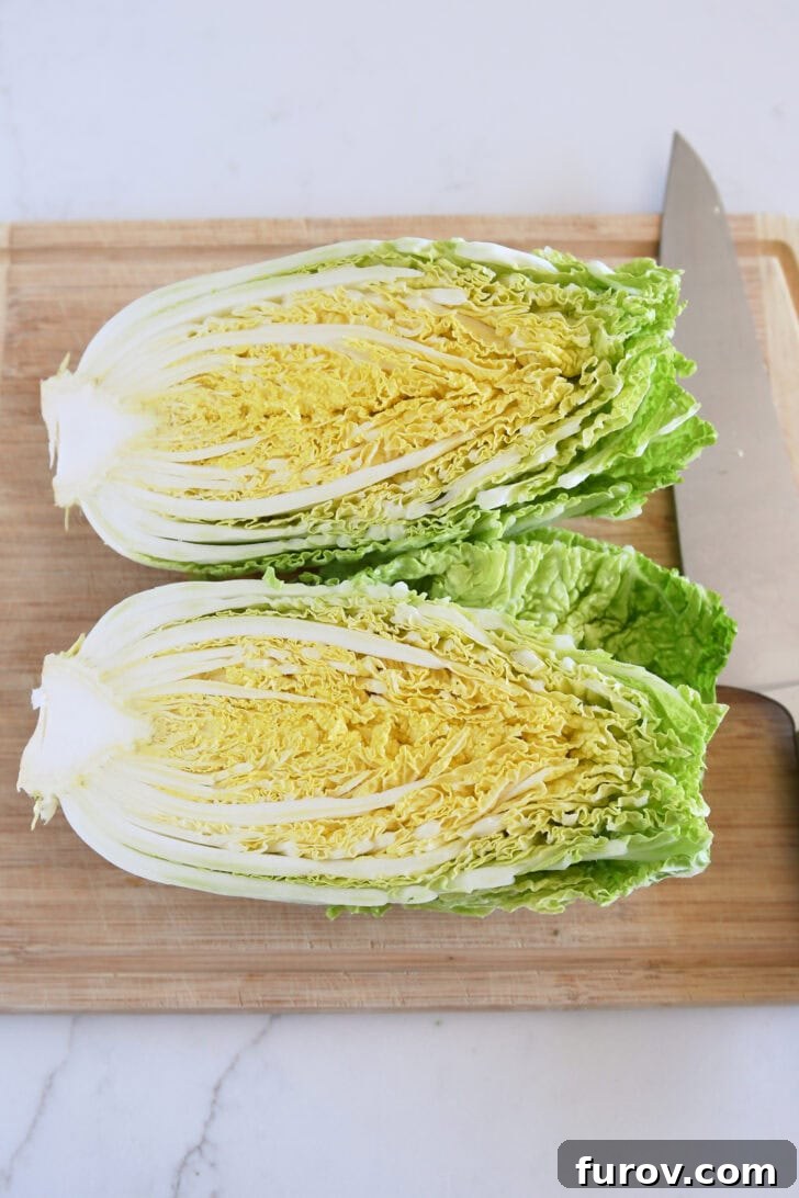 Napa cabbage cut in half on a rustic wood cutting board, ready for slicing.