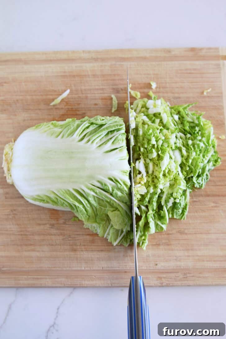 Napa cabbage thinly sliced and neatly piled on a wood cutting board, showcasing fine shreds.