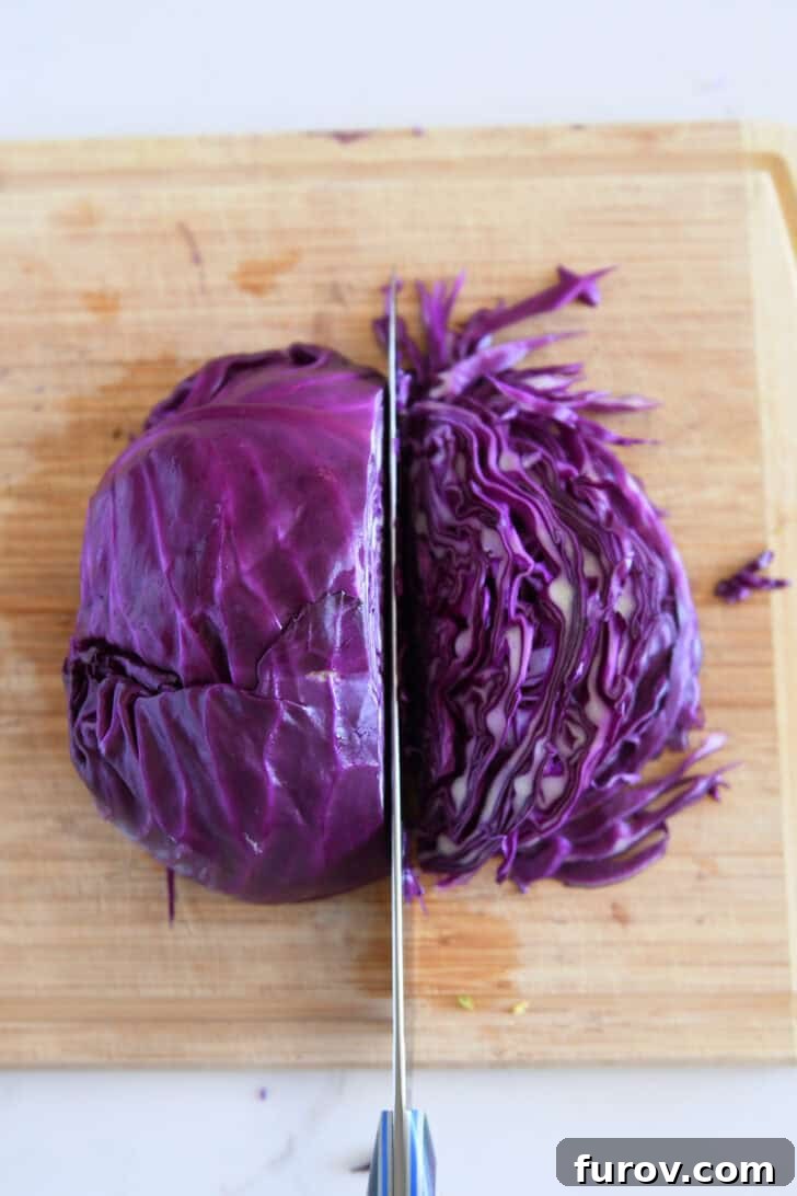 A chef's hand skillfully thinly slicing red cabbage on a wood cutting board.