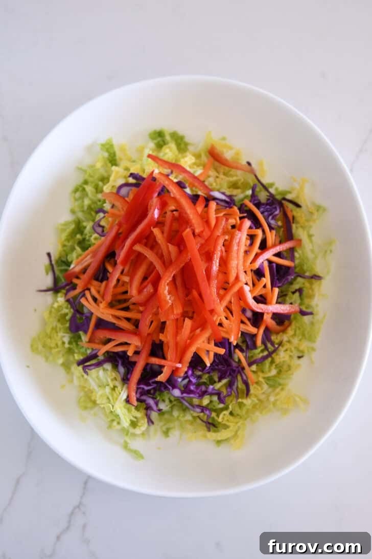 Julienned red peppers join matchstick carrots, red cabbage, and Napa cabbage in a white bowl, creating a colorful and inviting base.