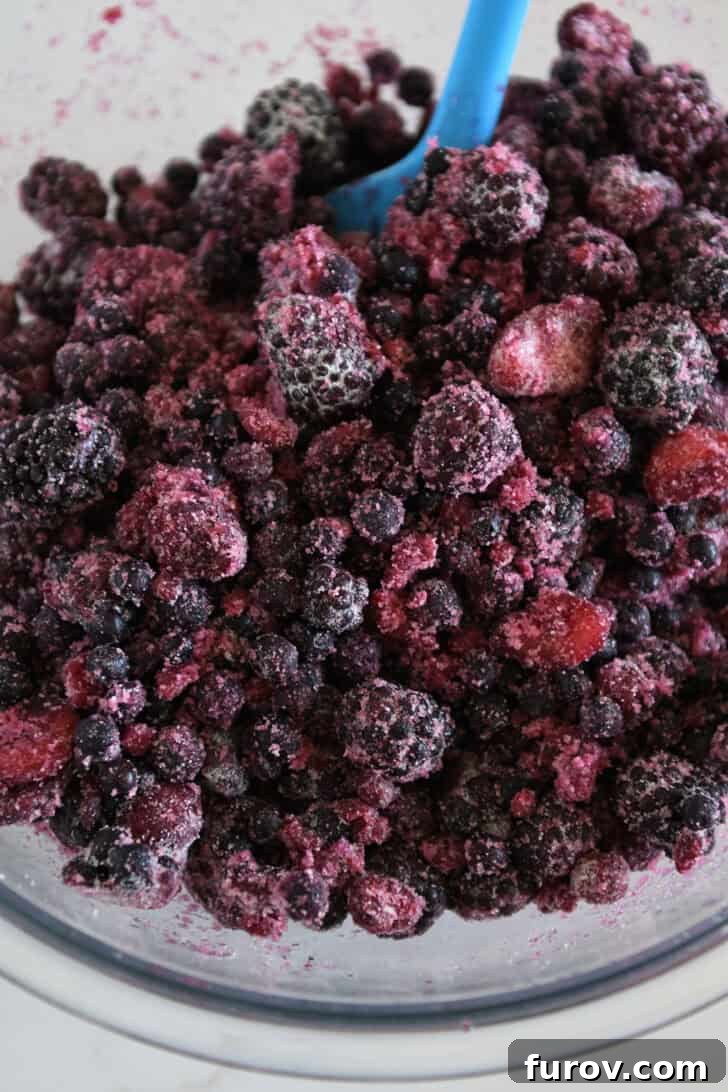 The Ultimate Triple Berry Cobbler with an Unforgettable Topping 4 Triple berry mixture gently tossed with sugar and flour, showcasing the glossy fruit coating that will soon transform into a luscious filling, all in a clear glass bowl.