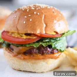 Homemade hamburger bun with juicy burger, lettuce, tomato and mustard.