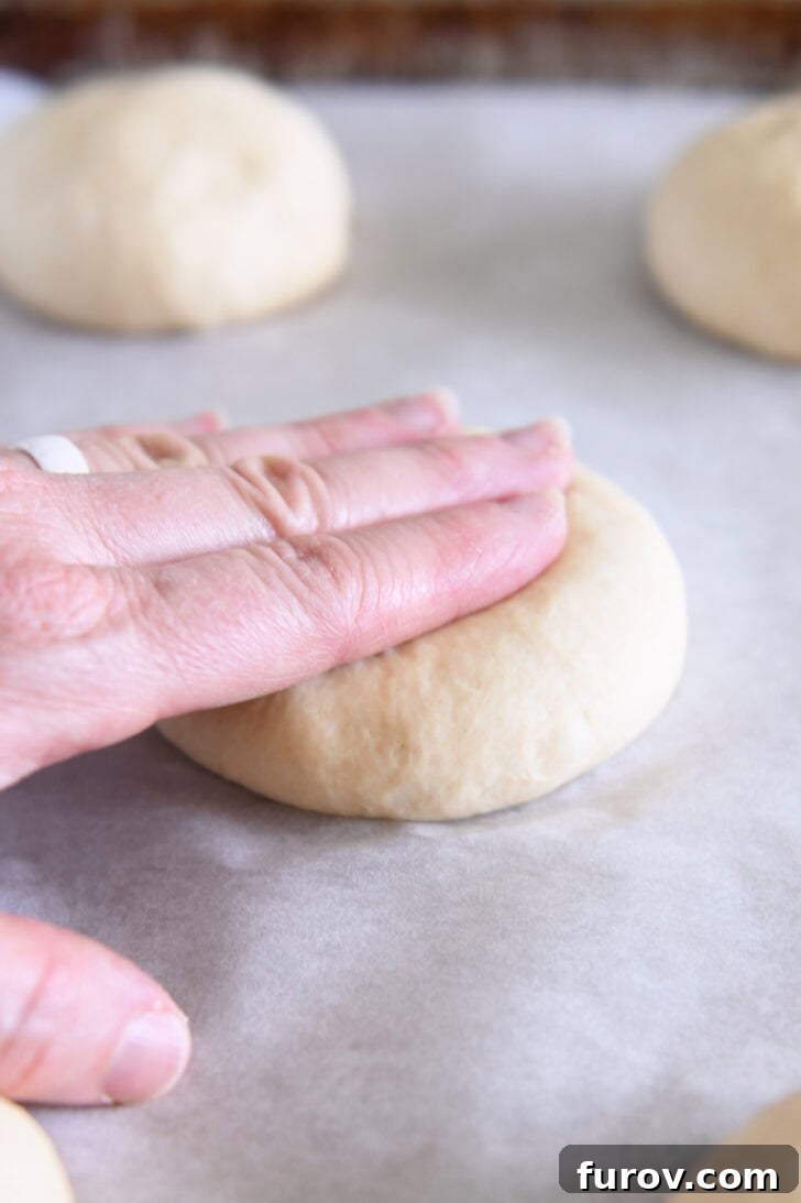 Pressing dough into thick disc shape for homemade hamburger buns.