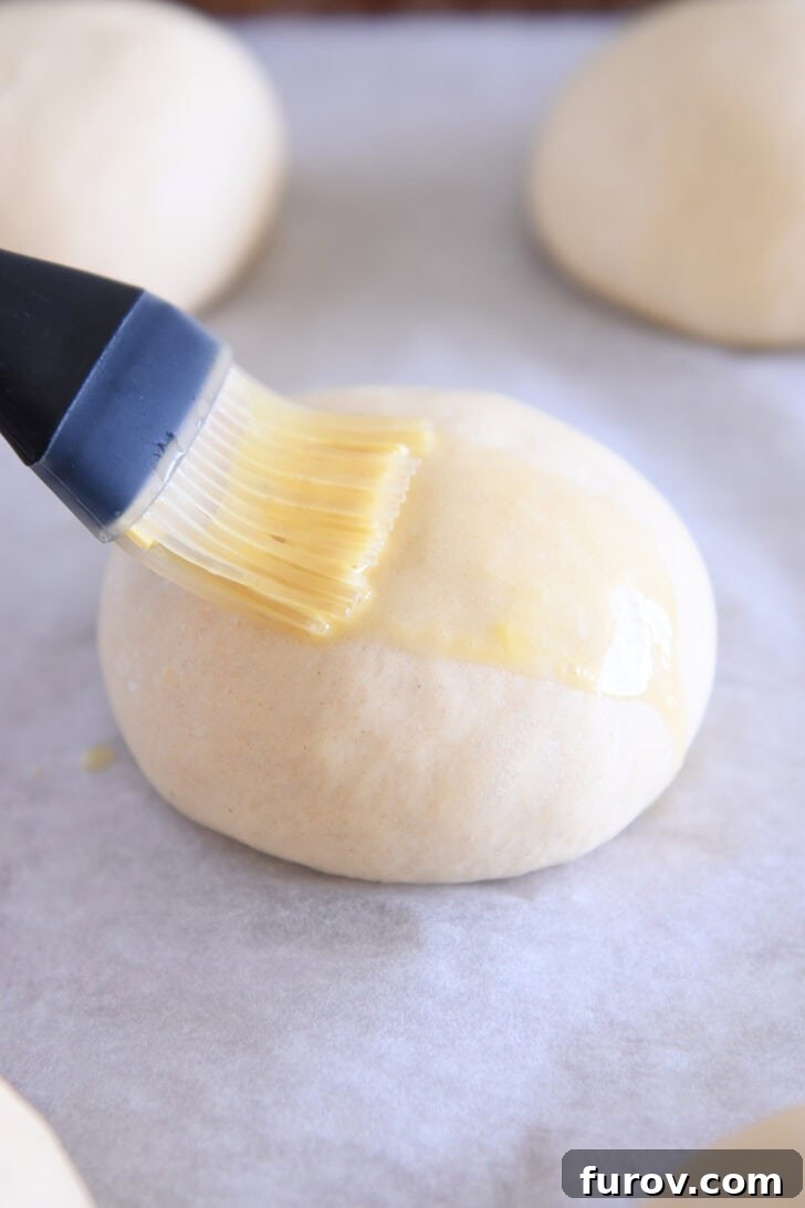 Brushing egg wash on top of hamburger bun dough with pastry brush.