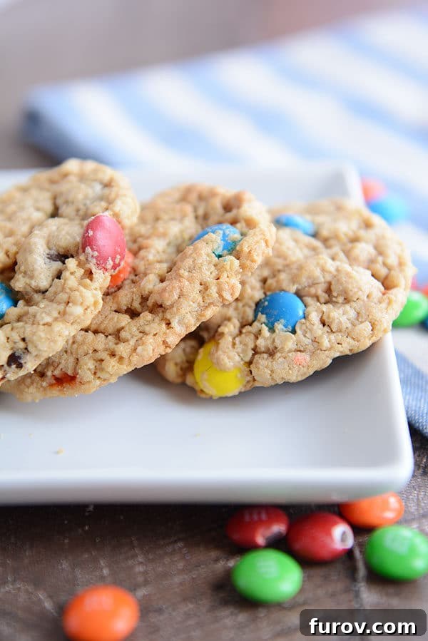 Epic One-Bowl Gluten-Free M&M Monster Cookies 2 A white tray with three oat M&M cookies and a few M&M's sprinkled around the side, showcasing their vibrant colors and inviting texture.
