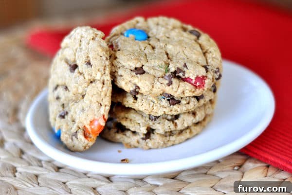 Epic One-Bowl Gluten-Free M&M Monster Cookies 9 A neatly stacked pile of M&M chocolate chip oat cookies resting on a pristine white plate, showcasing their inviting texture and colorful toppings.