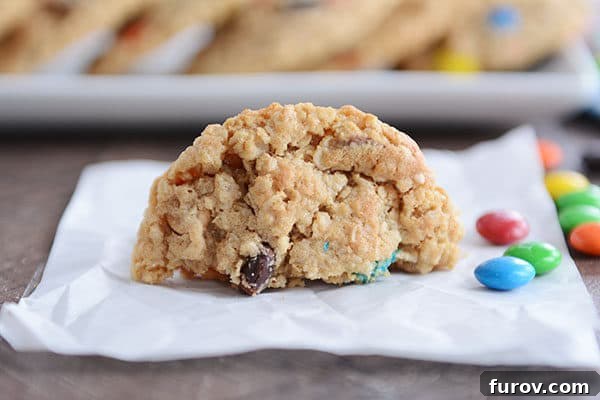 Epic One-Bowl Gluten-Free M&M Monster Cookies 5 A perfectly baked M&M cookie, halved to reveal its soft interior and rich texture, resting on parchment paper with a scattering of M&M's nearby.