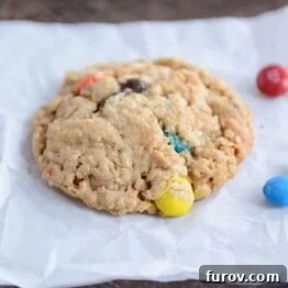 A single Monster M&M cookie, perfectly round and generously studded with colorful candies and chocolate chips.