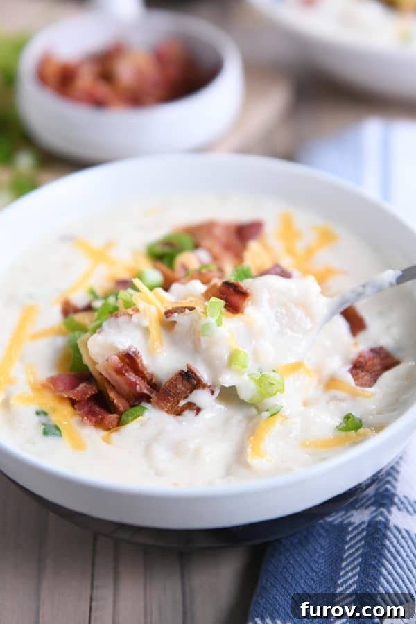 Spoon taking scoop out of loaded baked potato soup in white bowl.