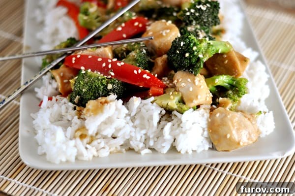 White platter with cooked white rice and sesame stir fry chicken, garnished with sesame seeds and fresh scallions.