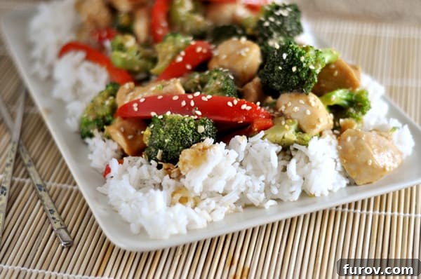 White rectangular platter with cooked white rice and sesame chicken and veggie stir-fry, presented neatly.