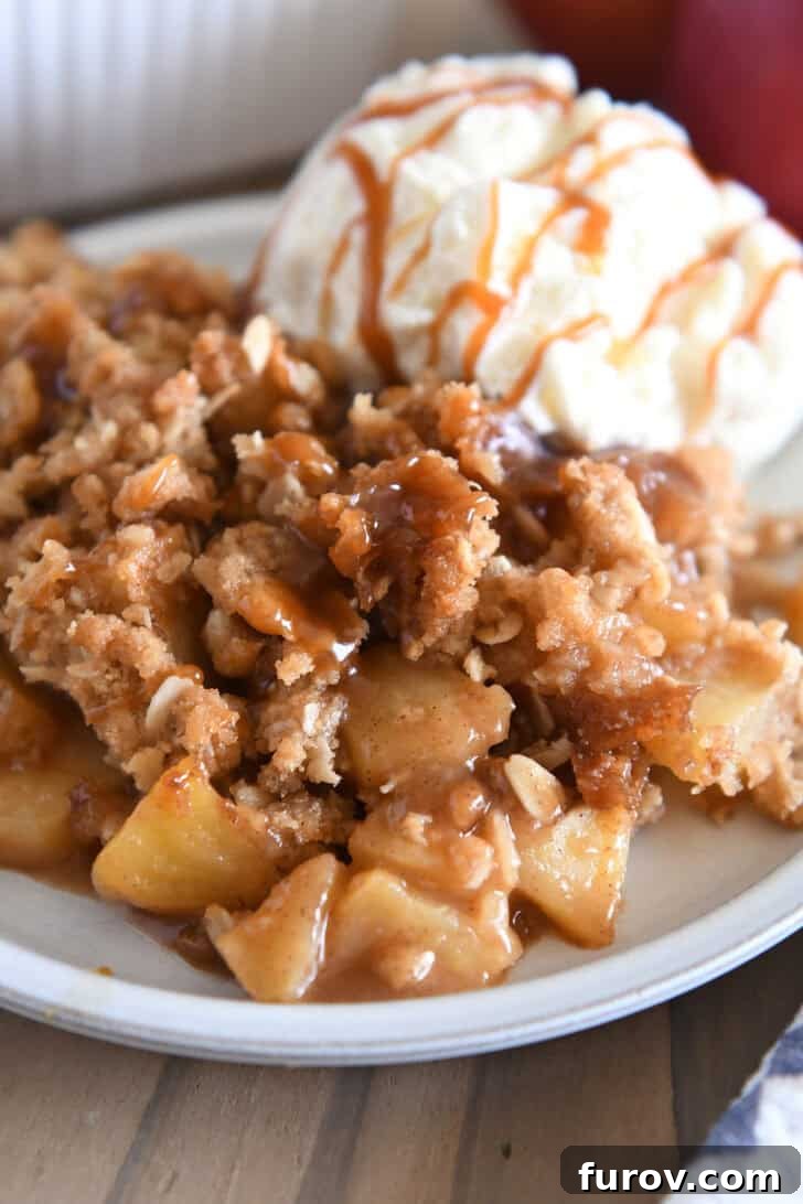 Gooey Caramel Apple Crumble 2 A warm serving of homemade caramel apple crisp on a gray plate, topped with a melting scoop of vanilla ice cream, ready to be enjoyed.